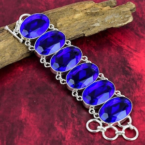 May include: A silver bracelet featuring six large, oval-shaped, blue gemstones. The bracelet has a toggle clasp.