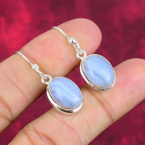 May include: A pair of silver earrings featuring oval, pale blue gemstones. The gemstones have a striped pattern and are set in a silver bezel. The earrings are on a silver hook.