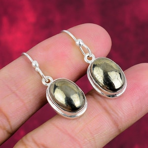 May include: A pair of silver dangle earrings with oval-shaped pyrite stones. The stones have a metallic gold color and a textured surface.