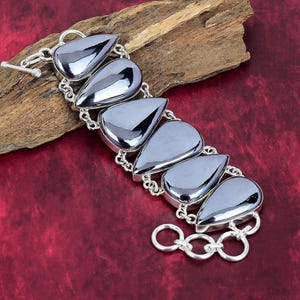 Puede incluir: Un brazalete de plata con un diseño de cadena y seis piedras de hematites negras en forma de lágrima.