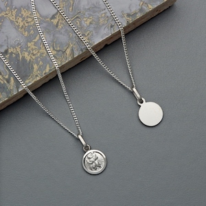 May include: Two silver necklaces with pendants. One pendant is a round disc, the other is a round pendant with a detailed image of a person.