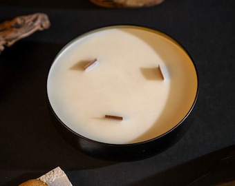 May include: A black candle with three wooden wicks in a black glass jar. Two gold scarab beetle figurines are on a piece of concrete. A black triangular prism is on a black surface.
