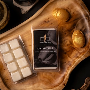 Puede incluir: Un juego de seis fundidos de cera de soja en un recipiente de plástico transparente. Los fundidos de cera son blancos y están empaquetados con una etiqueta negra que dice "HOUSE OF GEB COCONUT MILK COCONUT ALMOND VANILLA SUGAR MILK SOY WAX MELTS 4oz | 113.4g".
