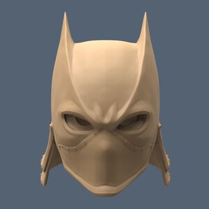 May include: A 3D printed model of a stylized mask with a pointed, bat-like design. The mask is beige and has a textured surface. The mask has a small, pointed nose and two large, almond-shaped eyes.
