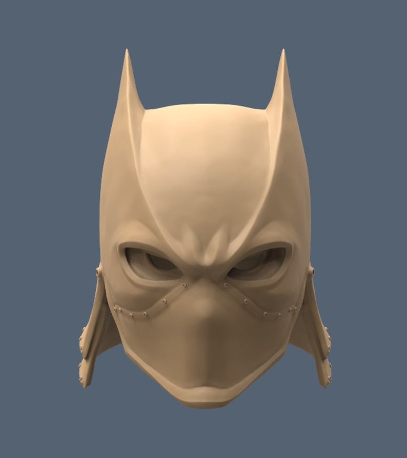 May include: A 3D printed model of a stylized mask with a pointed, bat-like design. The mask is beige and has a textured surface. The mask has a small, pointed nose and two large, almond-shaped eyes.