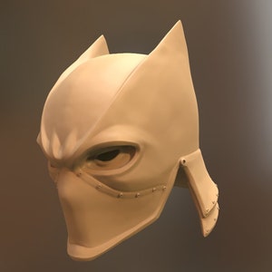 May include: A white plastic mask with a pointed, angular design. The mask has a raised, textured surface and a small, round eye opening.