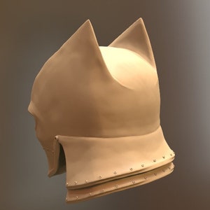 May include: A beige helmet with a pointed top and two ear flaps. The helmet has a textured surface and is decorated with small metal rivets.