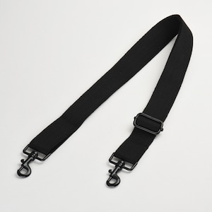 May include: Black adjustable shoulder strap with metal clasps. The strap is made of a woven fabric.