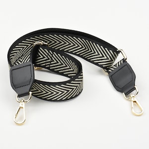 May include: Black and gold chevron patterned adjustable strap with gold hardware and a black leather accent.