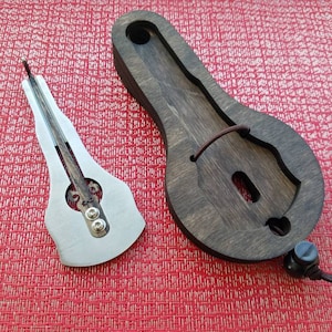 Op de afbeelding: Een zilverkleurig, handzaam muziekinstrument dat een 'duimpiano' of 'kalimba' wordt genoemd, met een houten koffer. Het instrument heeft een houten klankkast en een metalen resonator.
