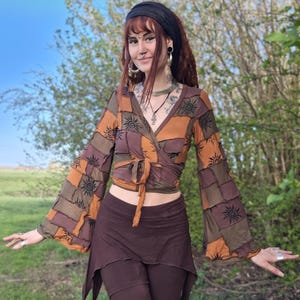 Op de afbeelding: Een wikkel top met klokmouwen en een bijpassende rok. De top heeft een patchwork ontwerp in bruin- en oranjetinten, met een zonnepatroon. De rok en broek zijn effen bruin van kleur. De outfit is in bohemian stijl.