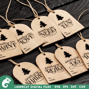 K&ouml;nnte beinhalten: Zehn h&ouml;lzerne Geschenkanh&auml;nger mit einem Weihnachtsbaumdesign und dem Text "Something you..." gefolgt von einem anderen Wort auf jedem Anh&auml;nger. Die W&ouml;rter sind: Want, Love, Need, Fun, Share, Read, Do, Wear.