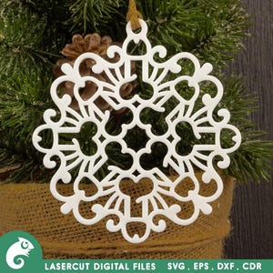 May include: White snowflake ornament with intricate cut-out design, hanging from a green pine branch.