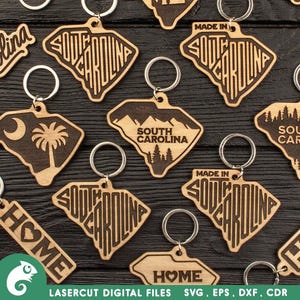 Puede incluir: Un conjunto de llaveros de madera cortados con láser que presentan el contorno del estado de Carolina del Sur. Algunos llaveros tienen las palabras "South Carolina" escritas dentro del contorno, mientras que otros tienen las palabras "Made in South Carolina". Algunos llaveros también tienen la palabra "Home" escrita en ellos.