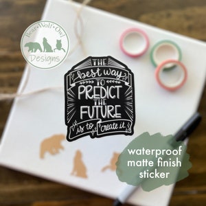 May include: Black and white sticker with the text "THE best way TO PREDICT THE FUTURE is to create it." The sticker has a chalkboard background and a white border. The sticker is on a white surface with a green and pink washi tape.