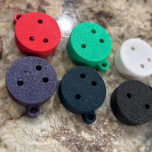 May include: Assortment of ten round, colourful, plastic buttons with three holes each. The buttons are in various colours, including brown, red, green, white, grey, and black.