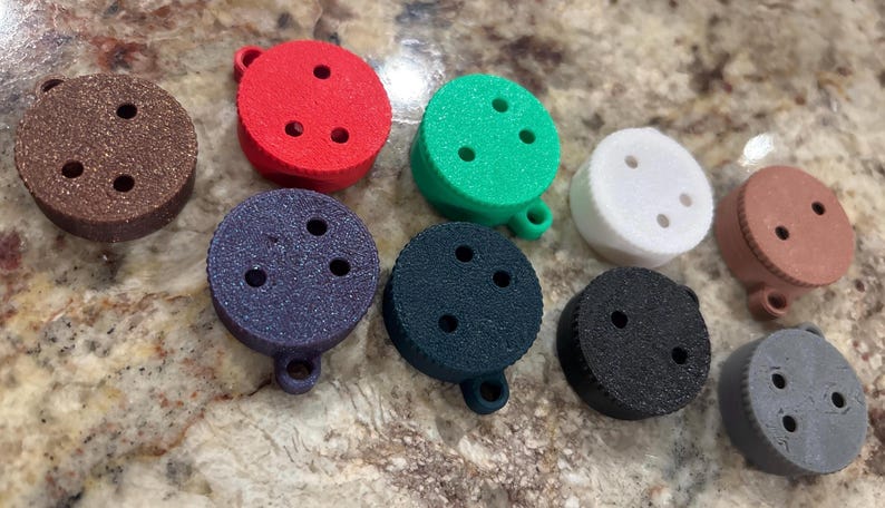 May include: Assortment of ten round, colorful, plastic buttons with three holes each. The buttons are in various colors, including brown, red, green, white, gray, and black.