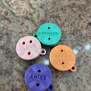 May include: Four small, round, colourful, scented discs with holes and a string attached. The discs are labelled "Anise", "Birch", "Clove", and "Cypress".