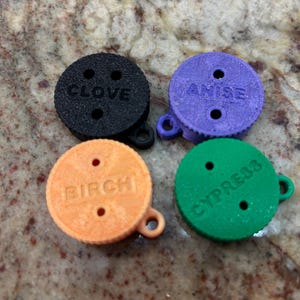 May include: Four round, colourful, plastic discs with holes and text. The discs are labelled "Clove", "Anise", "Birch", and "Cypress".