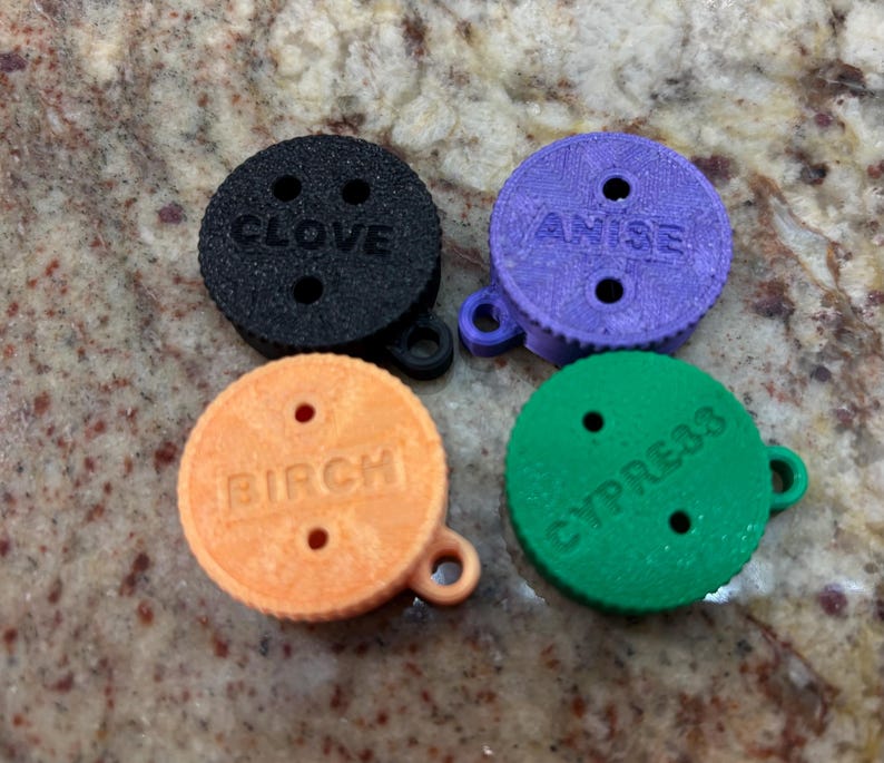 May include: Four round, colourful, plastic discs with holes and text. The discs are labelled "Clove", "Anise", "Birch", and "Cypress".