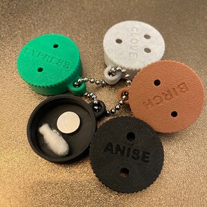 May include: Five round, plastic spice jars with screw-on lids. Each jar has a different spice name printed on the lid: "Anise", "Clove", "Thyme", "Curry", and "Cayenne". The jars are connected by a silver chain.