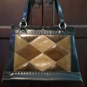 May include: A black leather handbag with a diamond-shaped patchwork design in shades of brown and tan. The bag has two top handles and a flap closure.