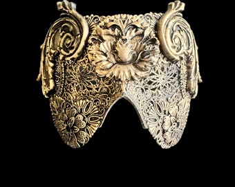 May include: A gold-colored metal crown with intricate floral designs and scrollwork. The crown is made of a delicate, filigree-like material.