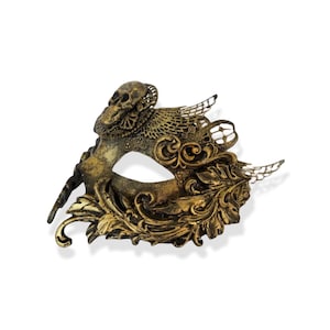Op de afbeelding: Een goud en bronskleurig masker met een schedel. Het masker heeft ingewikkelde filigraan- en bloemmotieven. Het metalen masker heeft een verweerde afwerking, waardoor het een vintage uitstraling heeft. Oogmasker.