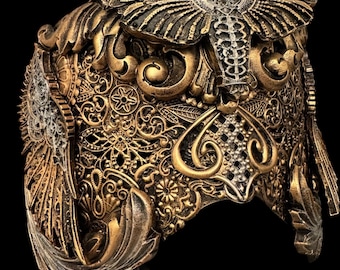 May include: A decorative headpiece featuring an intricate gold and bronze filigree pattern with ornate scrollwork and leaf motifs. A prominent moth figure with a skull-like marking on its thorax is centered at the top, flanked by wing-like side panels.