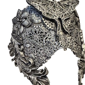 May include: Silver-toned headpiece with intricate floral, leaf, and lace-like patterns. A detailed moth adorns the top center. The headpiece has a curved shape and is likely made of metal.