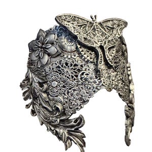 May include: Ornate silver-toned headpiece featuring a detailed butterfly and floral design. The headpiece has intricate filigree and scrollwork, with a prominent butterfly at the top. The overall design is gothic and fantasy-inspired.
