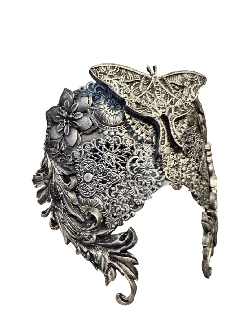 May include: Ornate silver-toned headpiece featuring a detailed butterfly and floral design. The headpiece has intricate filigree and scrollwork, with a prominent butterfly at the top. The overall design is gothic and fantasy-inspired.