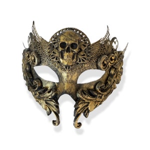 Op de afbeelding: Een goud en zwart maskerademasker met een schedelontwerp. Het masker heeft sierlijke details, waaronder vleugels en bloemmotieven. Het masker is gemaakt van een metallic materiaal en is ontworpen om te worden gedragen tijdens een gemaskerd bal of kostuumfeest.