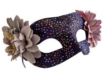 May include: A purple masquerade mask with rhinestones and two fabric flowers, one in a light gray and the other in a light pink.