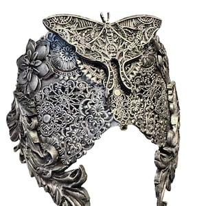 May include: A silver-toned headpiece with intricate floral, leaf, and lace-like patterns. A detailed butterfly design is centered on the crown. The headpiece has a gothic or fantasy aesthetic.
