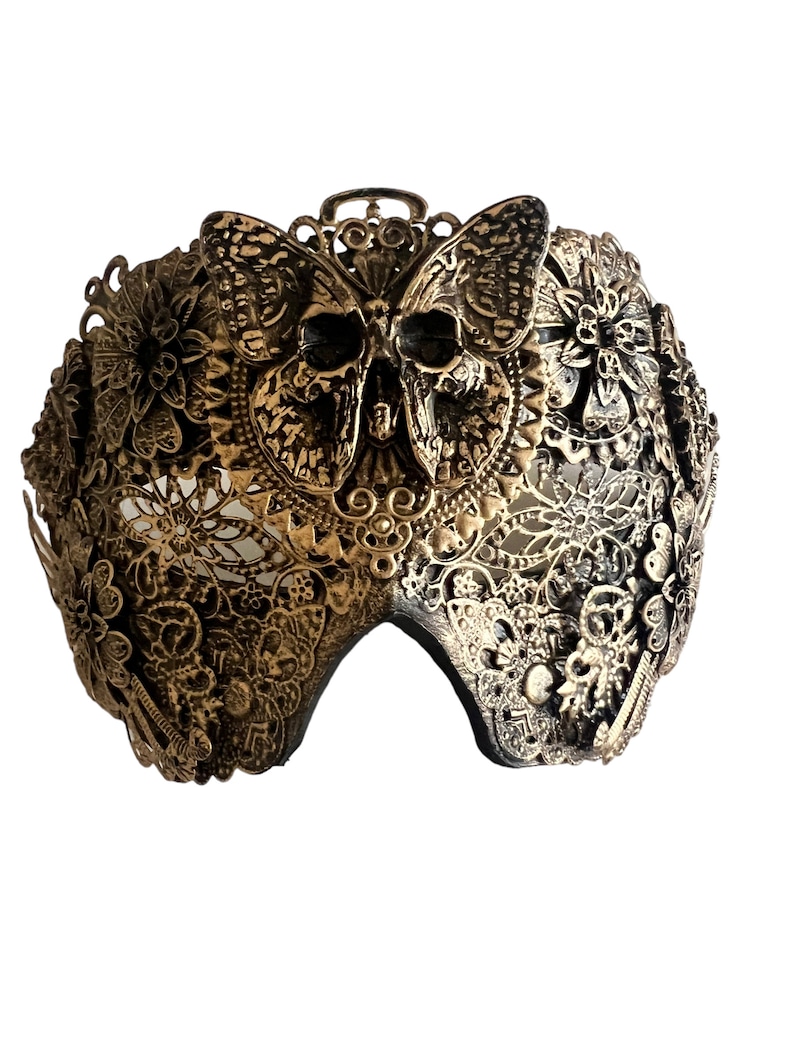 Puede incluir: Una m&aacute;scara de carnaval dorada con un dise&ntilde;o de calavera y mariposa. La m&aacute;scara est&aacute; hecha de metal y tiene un dise&ntilde;o delicado e intrincado.
