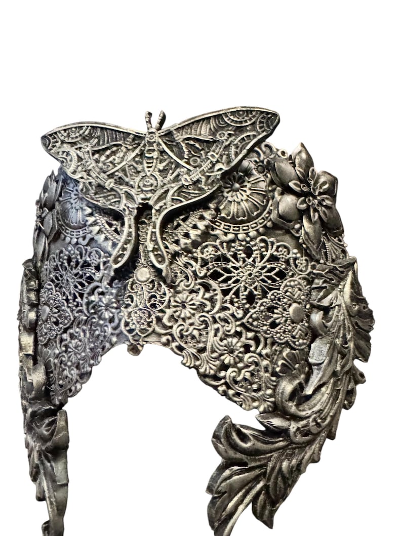 May include: Silver-colored headpiece with intricate filigree and floral designs. A large moth is centered on the crown. The headpiece has a detailed, ornate appearance, with a vintage or fantasy aesthetic.