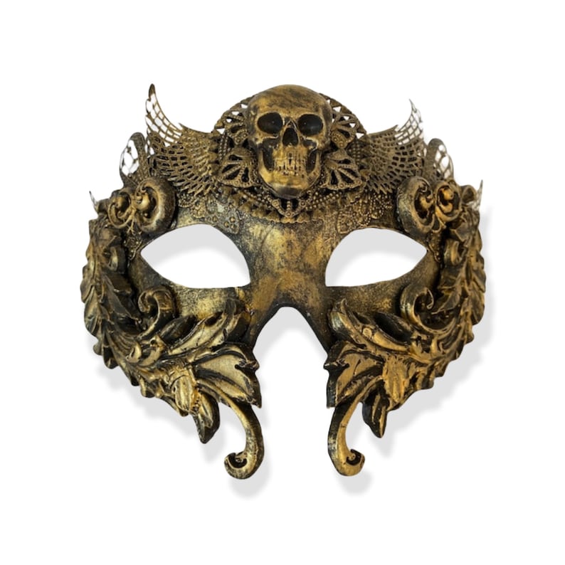 Op de afbeelding: Een goudkleurig masker voor een gemaskerd bal met een schedelontwerp in het midden. Het masker heeft ingewikkelde bloemen- en filigraan details, oogopeningen en een gebogen vorm. Waarschijnlijk gemaakt van metaal of een vergelijkbaar materiaal.