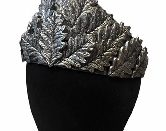 May include: A silver crown made of oak leaves. The crown is on a black mannequin head.