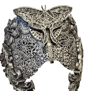 May include: A silver-colored headpiece with intricate floral and butterfly designs. The headpiece features detailed filigree and embossed patterns, creating a delicate and ornate appearance. The butterfly is centered on the headpiece.