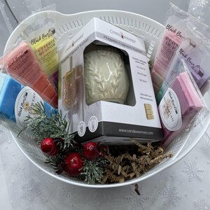 May include: A white ceramic plug-in fragrance warmer with a floral design, surrounded by various scented wax melts in a white wicker basket. The wax melts are labeled with names like "Butterfly Meadow", "Hawaiian Ocean", and "Peony in Pink".