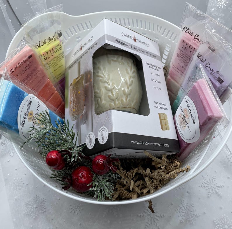 May include: A white ceramic plug-in fragrance warmer with a floral design, surrounded by various scented wax melts in a white wicker basket. The wax melts are labeled with names like "Butterfly Meadow", "Hawaiian Ocean", and "Peony in Pink".