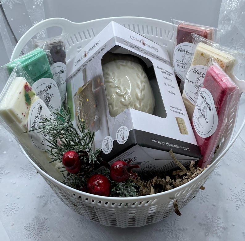 May include: A white wicker basket filled with a variety of scented wax melts and a white ceramic plug-in fragrance warmer. The wax melts are in various colors and have different scents, including "Blackberry & Bay Leaf" and "Cranberry Prosecco". The warmer is in a box with the text "Plug-in Fragrance Warmer" on it.
