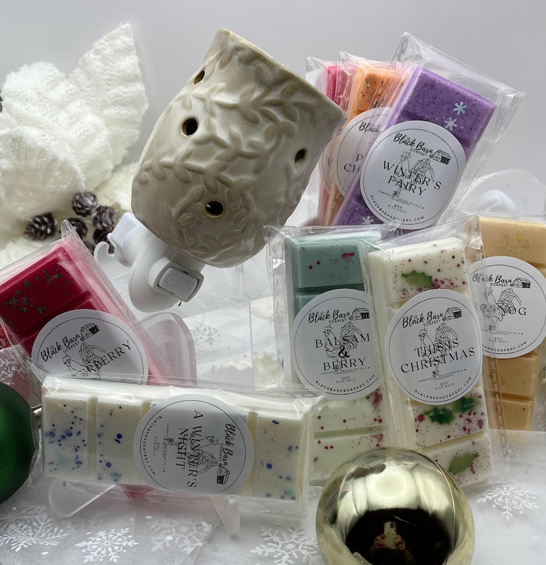 May include: A white ceramic wax warmer with a leaf design, surrounded by various scented wax melts in clear packaging. The wax melts have different scents, including "Winter's Party", "This is Christmas", "Balm & Berry", and "A Winter's Night".