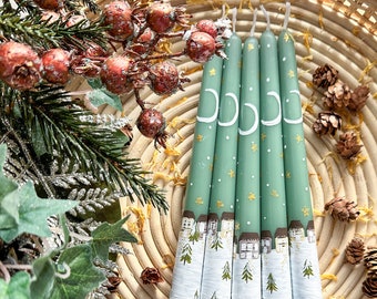 May include: Five green taper candles with a white and gold winter scene design. The candles are decorated with a crescent moon and stars.