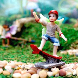 May include: A miniature fairy figurine wearing a red helmet and blue jeans, riding a red skateboard with green wings. The fairy is standing on a gray stone platform.