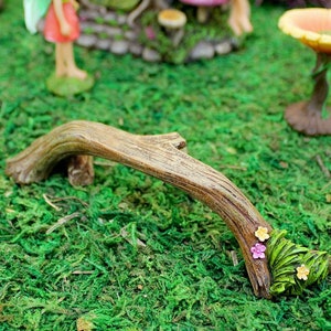 May include: A miniature wooden bridge with a natural brown finish and green leaves with pink and yellow flowers. The bridge is perfect for a fairy garden or miniature landscape.