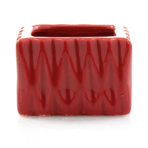 May include: A red ceramic planter with a textured, geometric design. The planter has a white rim and is rectangular in shape.
