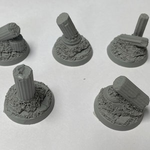 May include: Five gray plastic miniature bases with broken columns and rubble. The bases are designed for tabletop games and role-playing games.