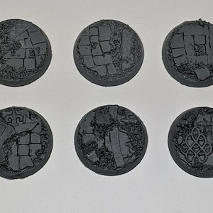 May include: Ten round, grey plastic bases with a textured surface resembling cracked pavement. The bases are designed for miniature wargaming.